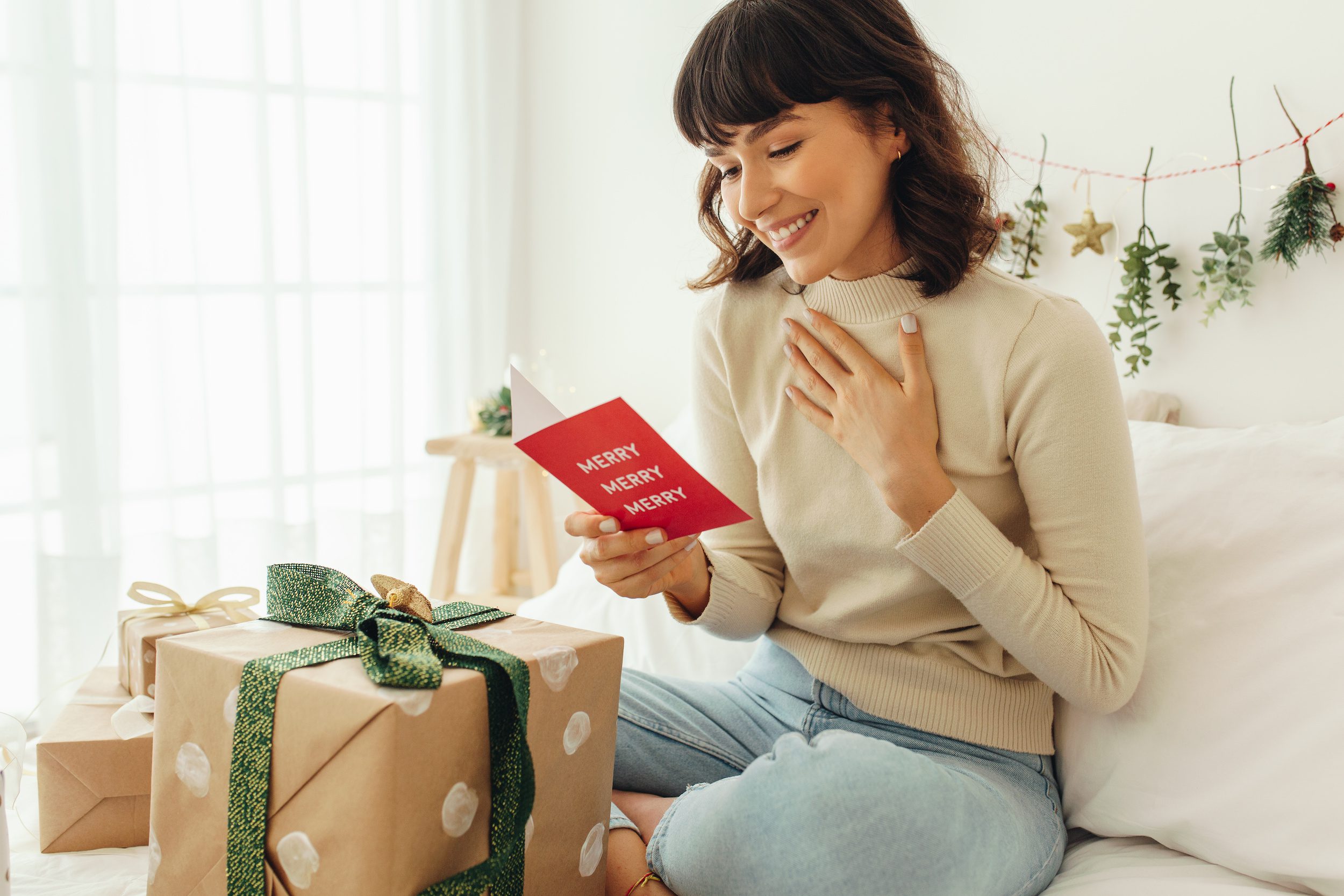 Close up of woman sitting on bed with Christmas present. Smiling woman holding a Christmas card.